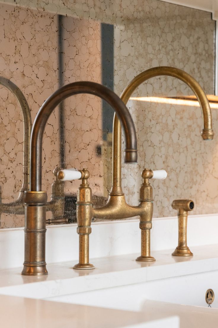 Brass kitchen faucet set on a countertop with a mirror in the background
