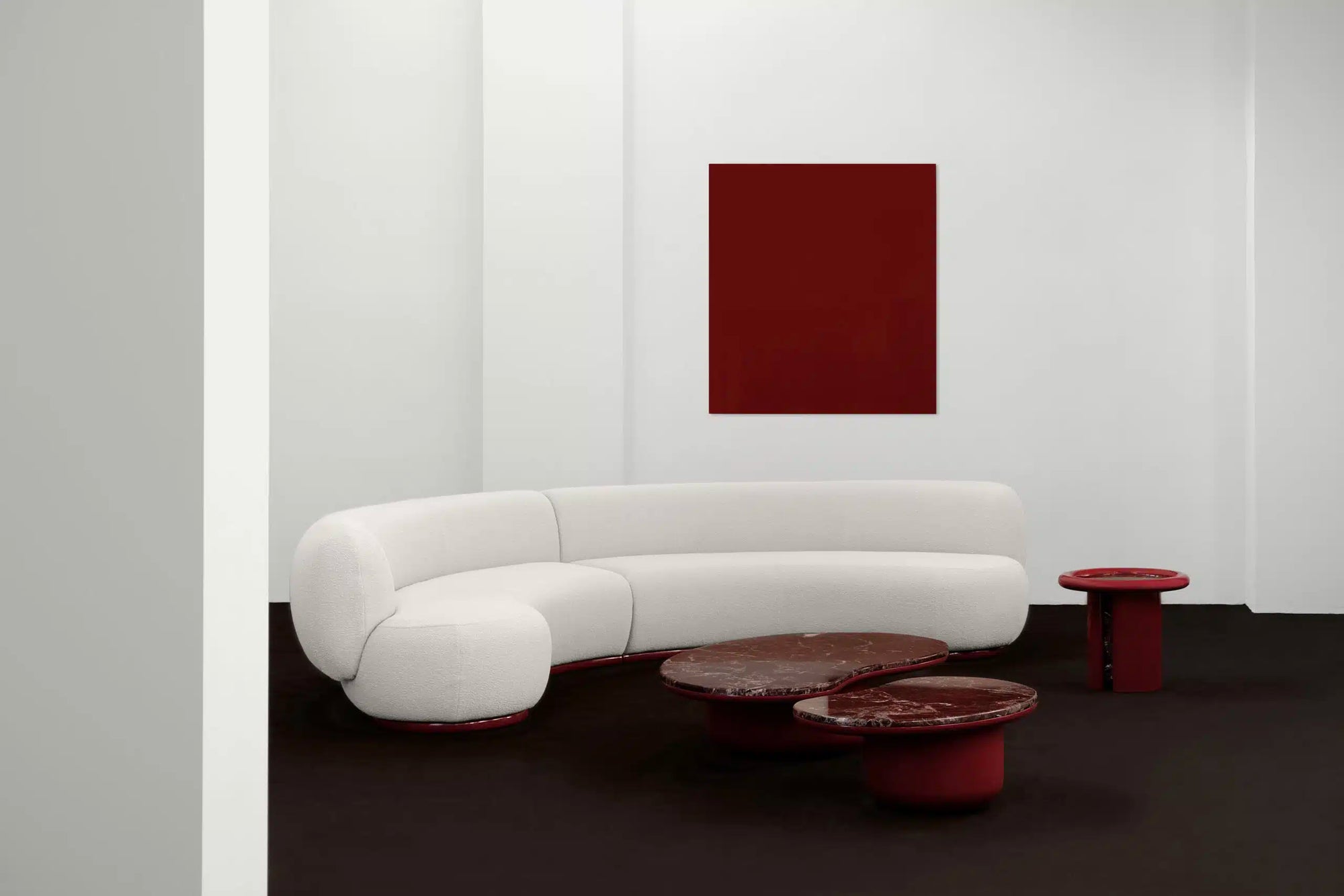 Modern white curved sofa with red marble coffee table and abstract painting in a minimalistic room.