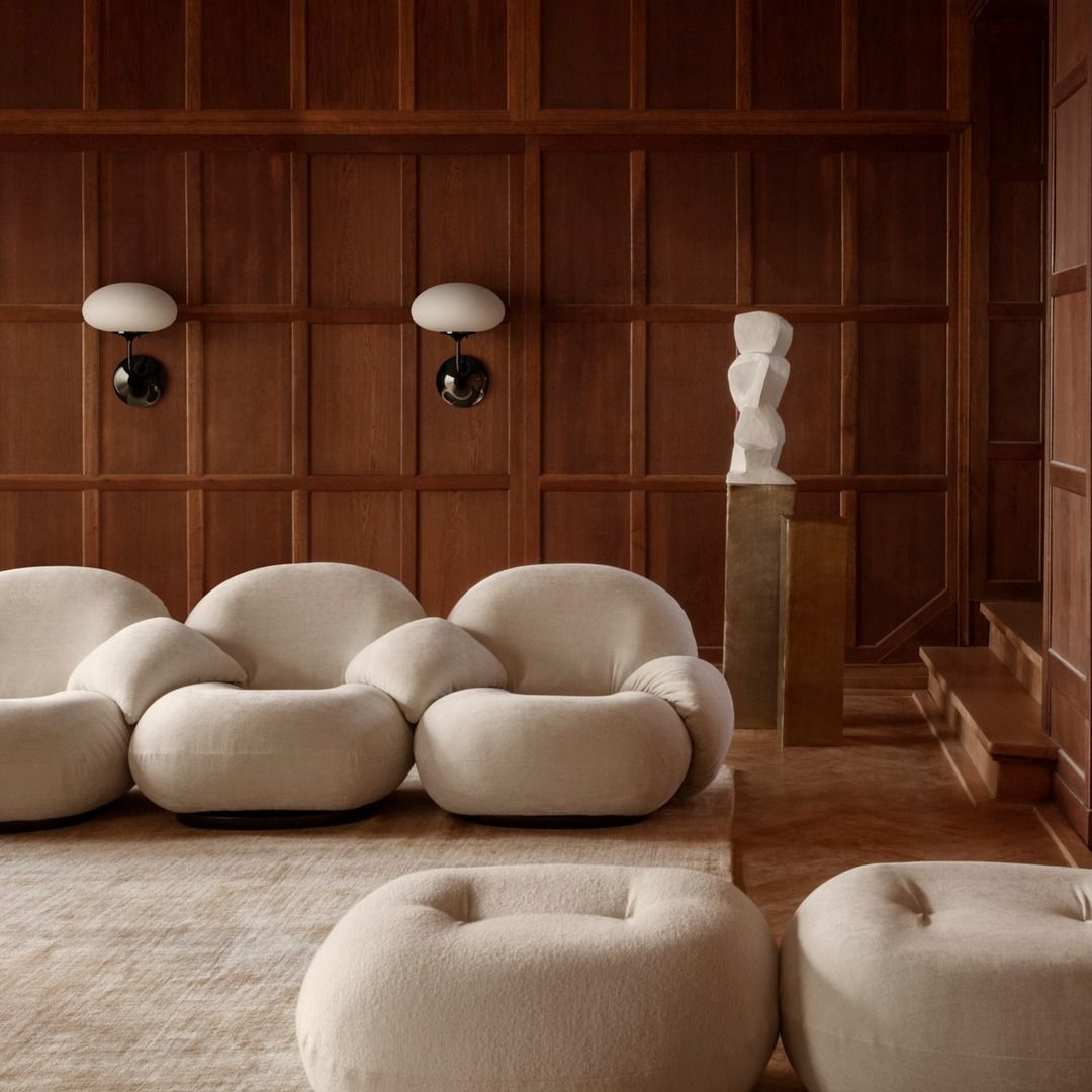 Beige modern chairs and sofa in a room with wooden paneling and wall sconces