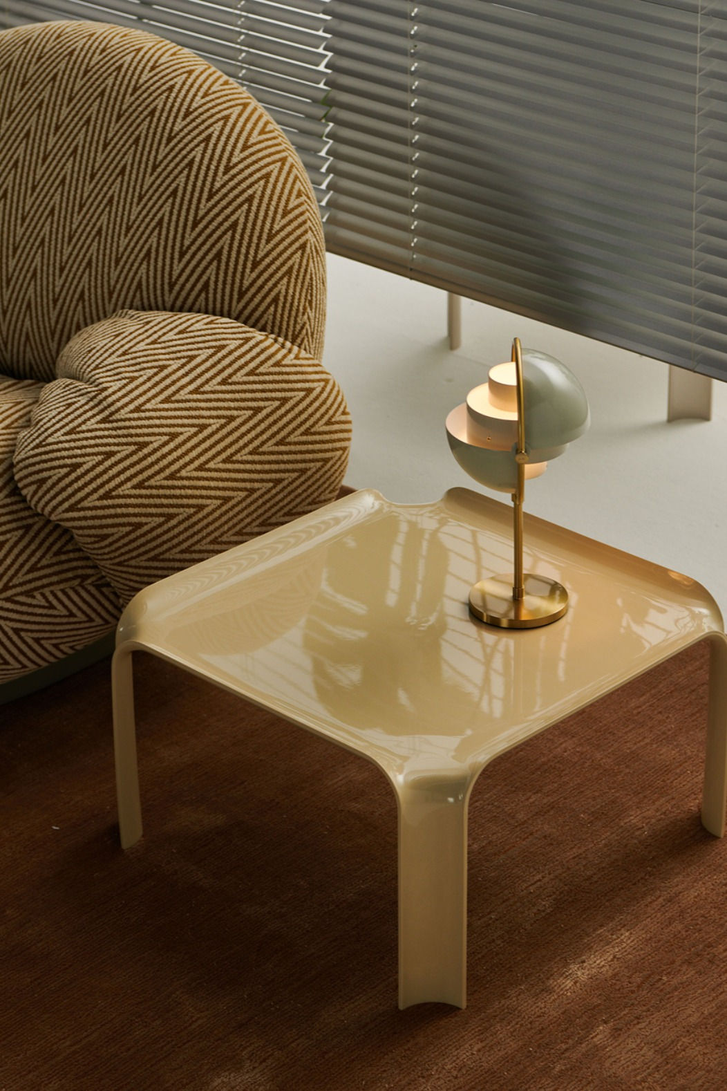 Beige Gubi side table with a decorative lamp next to a textured armchair.