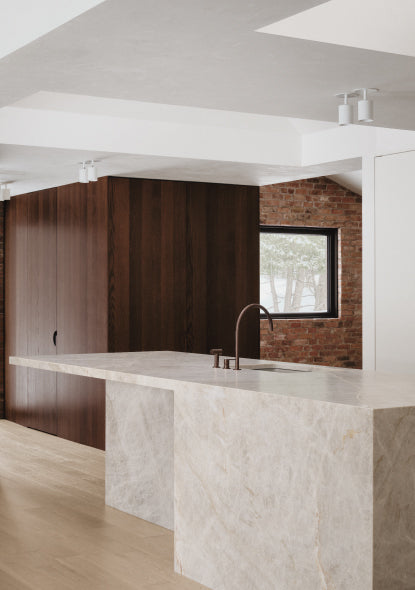 Modern kitchen with marble island and wooden cabinets and bronze taps