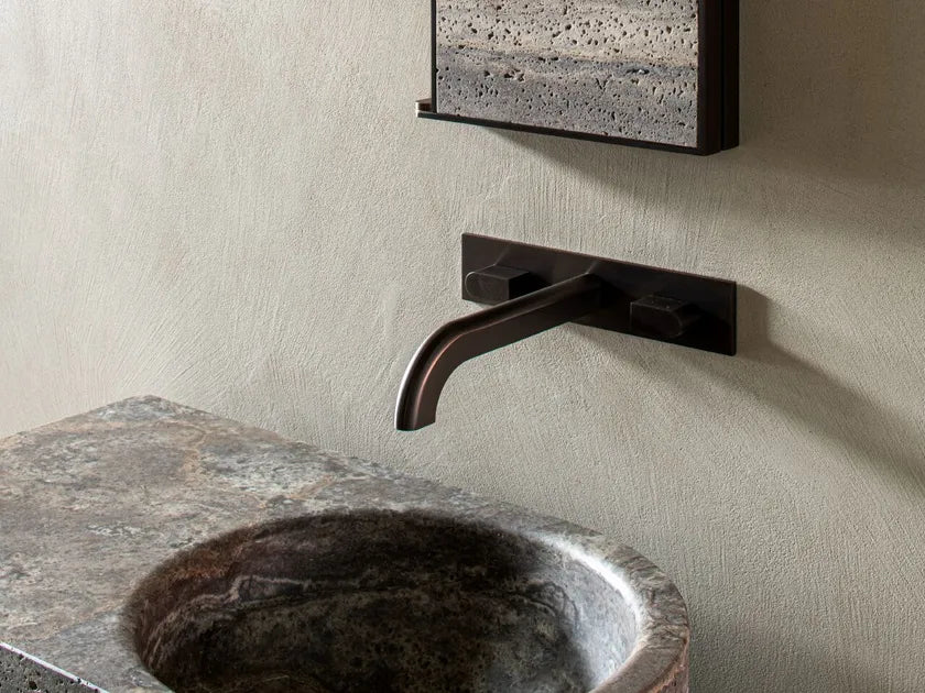 Dark bronze faucet on a stone sink with a textured wall in the background