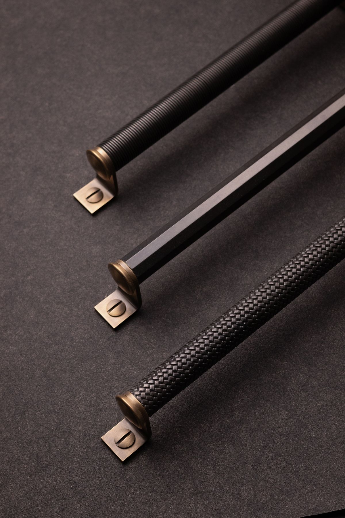 Three black metal handles with textured grips and gold accents on a dark background
